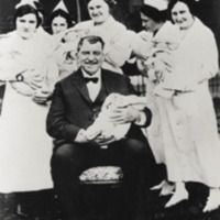 Russell Conwell, seated, holding a baby, surrounded by smiling nurses also holding babies