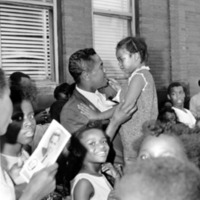 Georgie Woods (1927-2005) Civil Rights Leader and Broadcast Pioneer holding up a child in a crowd.